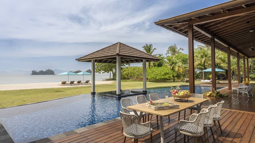 Pool deck with dining table, pool, covered lounge area and beach view