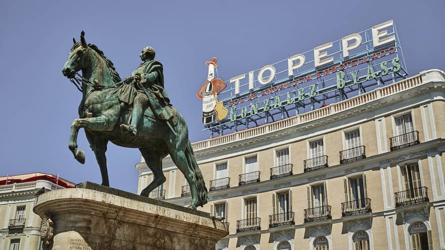 A statue of King Charles III of Spain on horseback in front of the Tio Pepe neon sign. The sign is on a sunny roof.