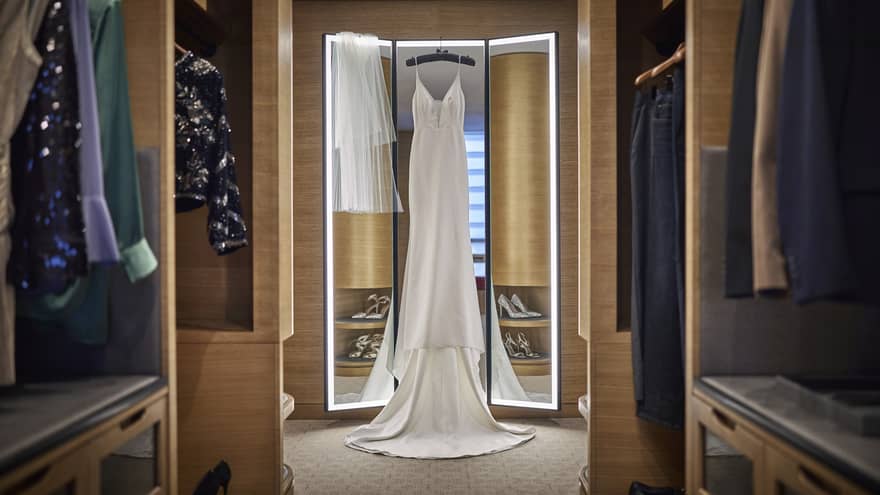 A wedding dress next to mirror in a large closet.