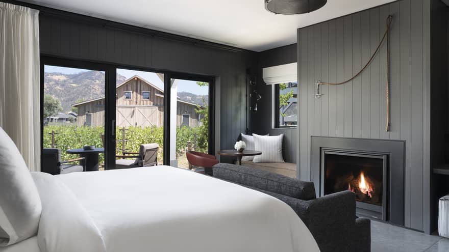 Luxury resort room with a king bed, cozy fireplace, vineyard view, seating area and outdoor patio facing rustic barn and mountains