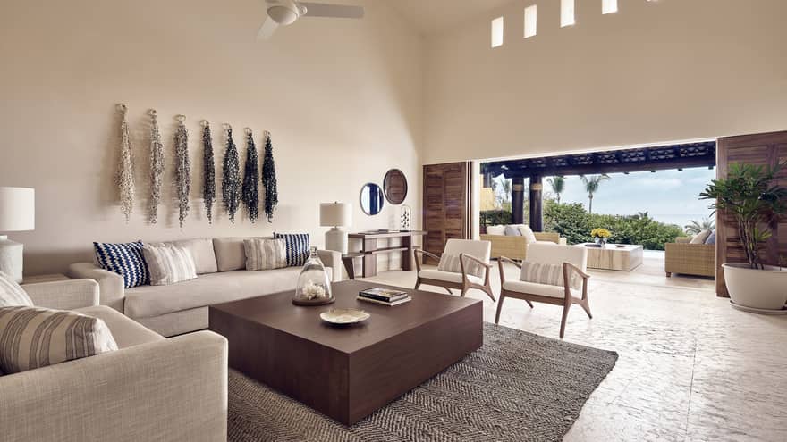 White linen sofas around large wood coffee table in bright living room, open patio wall