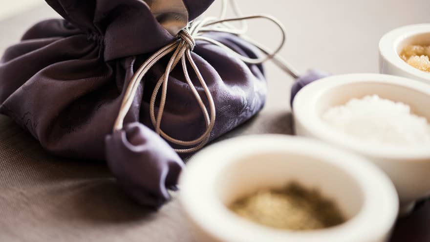 Dark silk pouch with tie behind small white ceramic bowls with spa salts