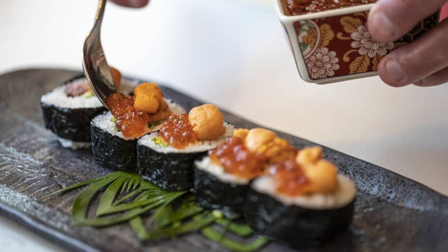 A close up of handing garnishing sushi rolls with caviar
