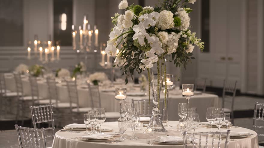 One formally set white rectangular table and candelabras, one round table and white floral centerpiece 