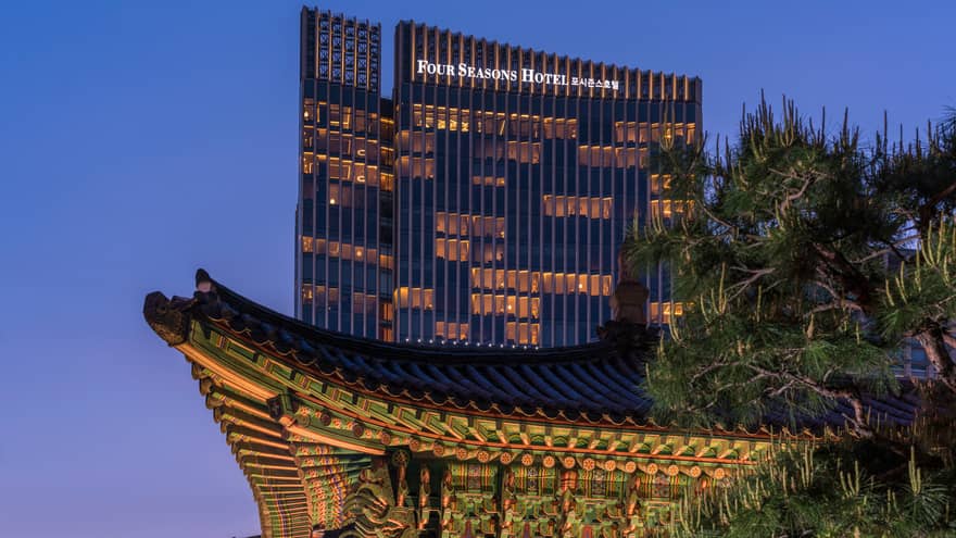 Four Seasons Hotel Seoul modern glass high rise with lights towering over traditional building at night