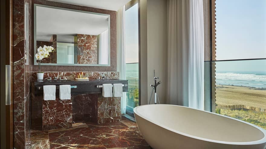 Signature Suite bathroom with deep soaker tub in front of window with ocean view, brown marble floor, wall