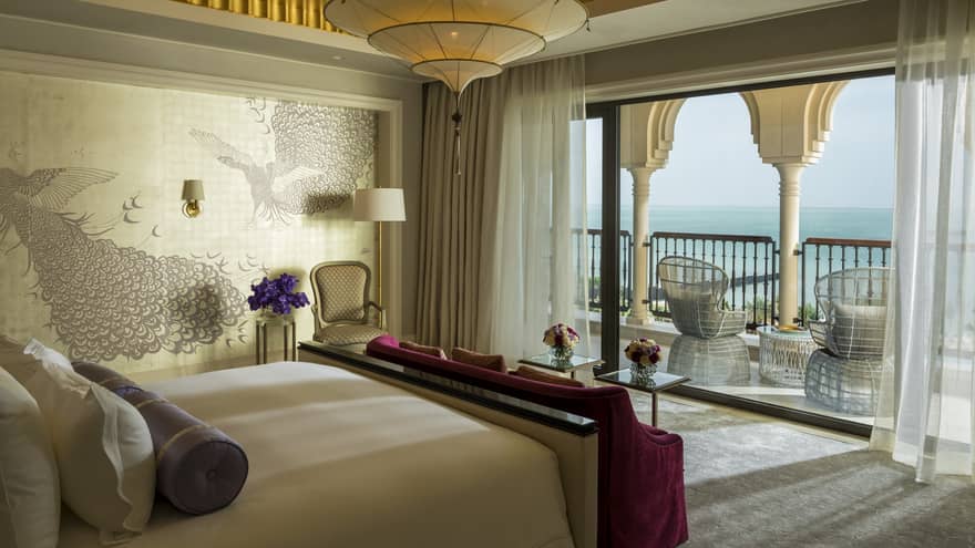Bedroom suite with decorative wallpaper, red velvet bench, patio with white pillars, wicker chairs