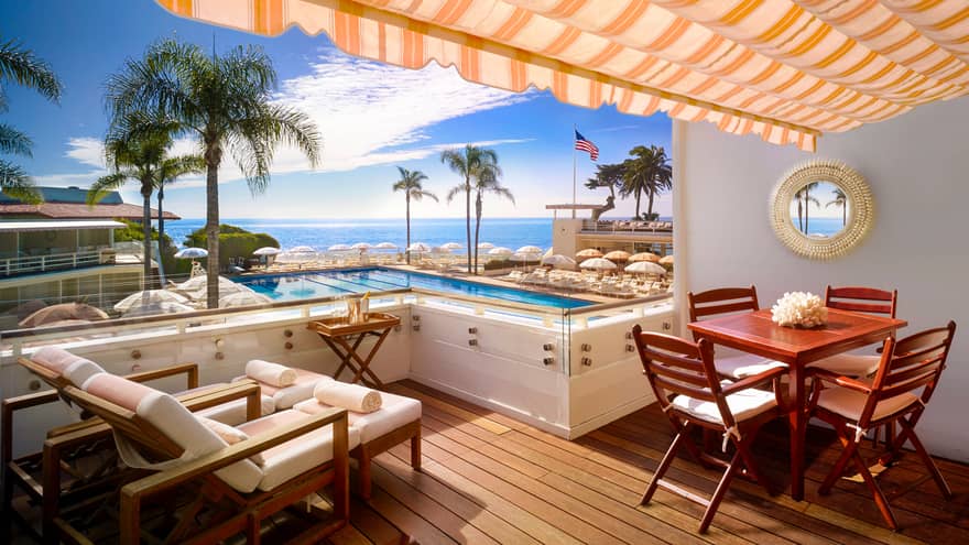 Lounge chairs, table on Cabana Club patio under striped orange awning, overlooking pool