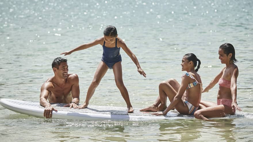 A family sitting on a large surf or paddleboard.