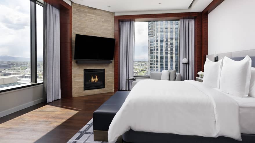 Corner guest room at Four Seasons Hotel Denver. City views through two large windows, king bed, fireplace, wall-mounted TV.