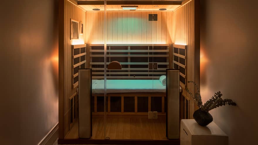 Wooden infrared sauna with lowlighting, side table with vase of eucalyptus 