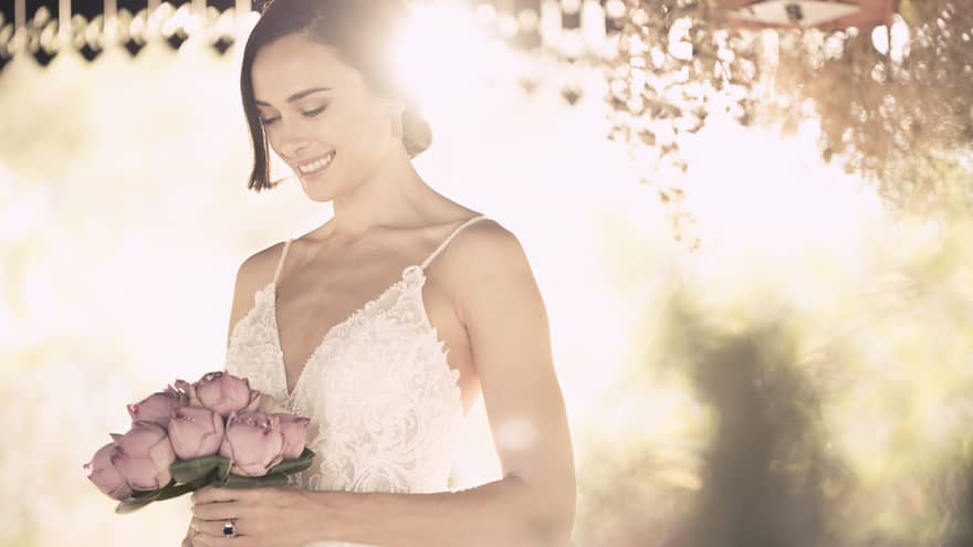 Sun streams down behind bride holding wedding bouquet with pink roses