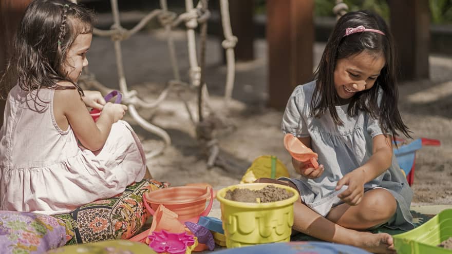 Two young girls play in the sand at Lutong Kids Club