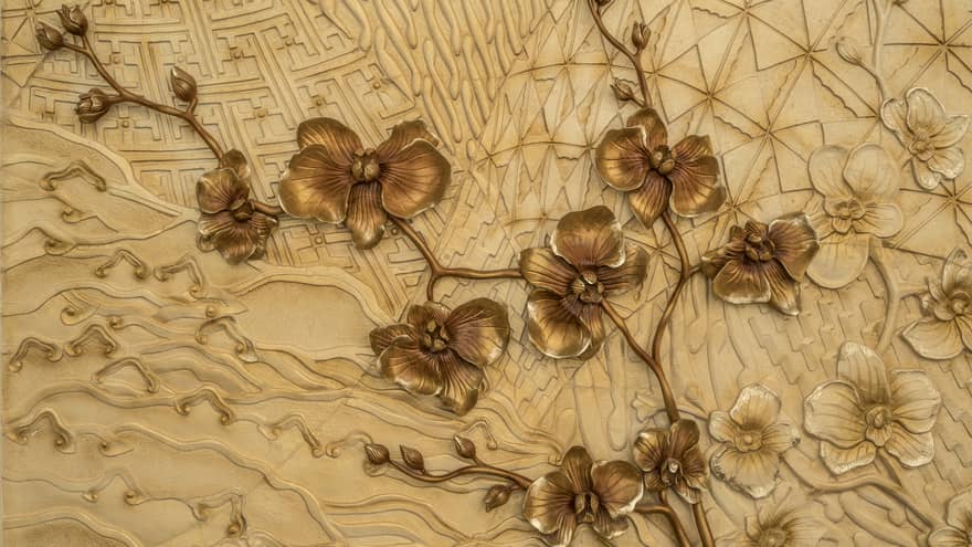 Close-up of batik design with metal bronze-coloured flowers sprouting across a tan background of varying bas-relief patterns.