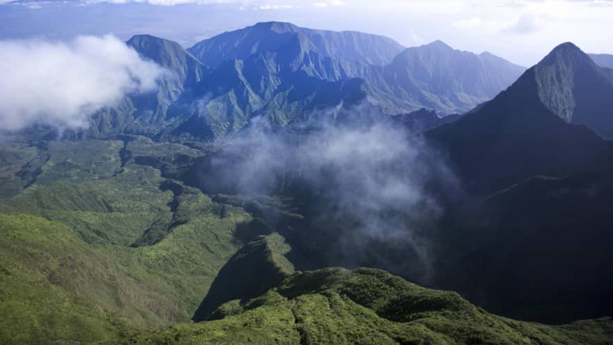 Clouds hover over green volcanic mountains