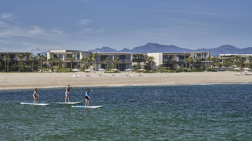 Three people on paddle boards in the water with a hotel behind them.