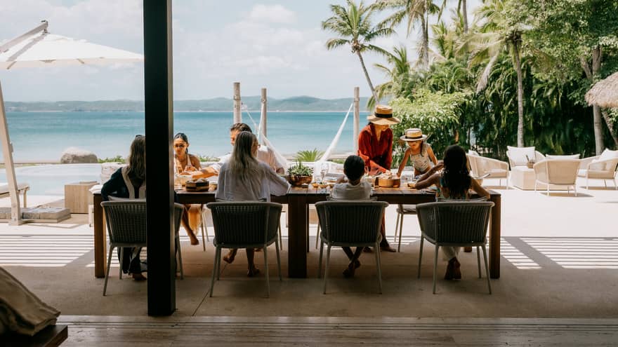 A group of people enjoy a meal in an outdoor dining setting looking out over the beach and ocean.