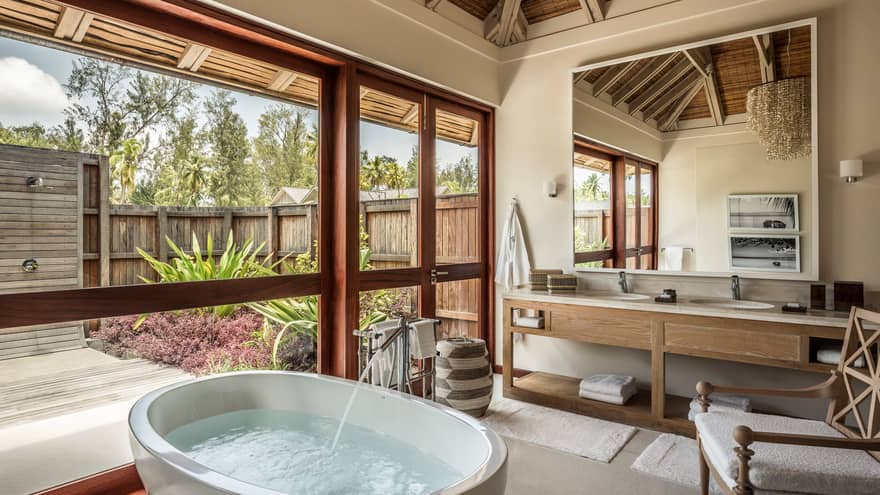 Water filling round soaking tub under window in bright bathroom