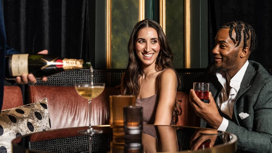 A man and woman drinking at a booth in a dim restaurant.