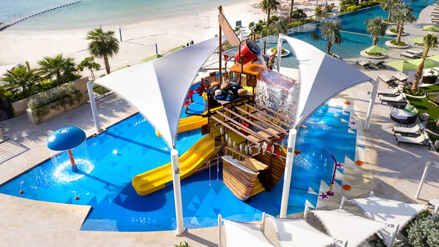 A large orange waterslide built into a faux pirate ship descending into a crystal blue pool of water.