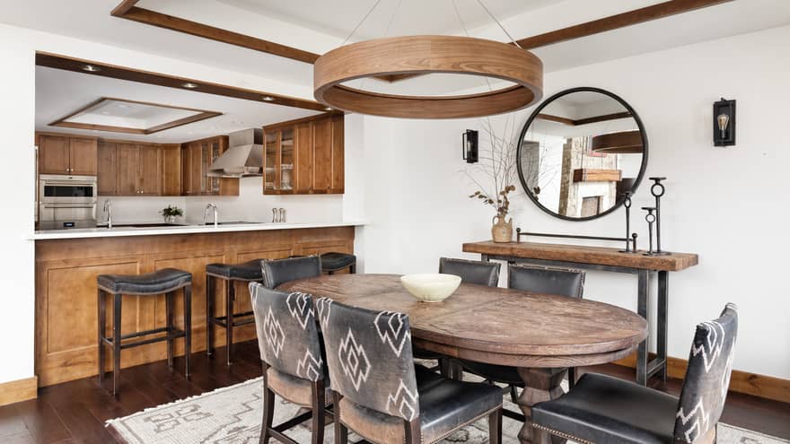 Mountain chic dining room with a rustic touch, featuring a wooden table, six leather chairs and open view to a kitchen with wood cabinetry