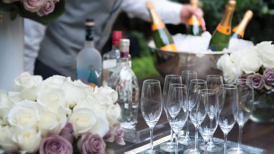 Close-up of white and purple roses, empty Champagne glasses on tray in front of ice bucket, bottles