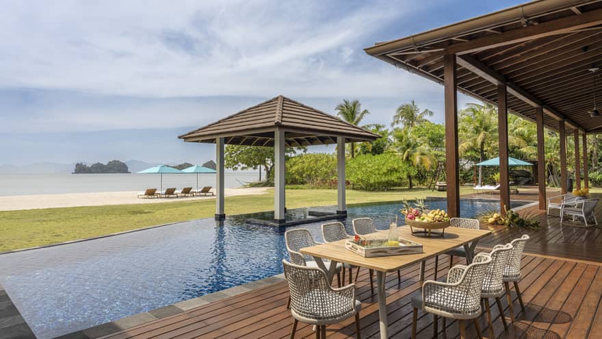 Pool deck with dining table, pool, covered lounge area and beach view