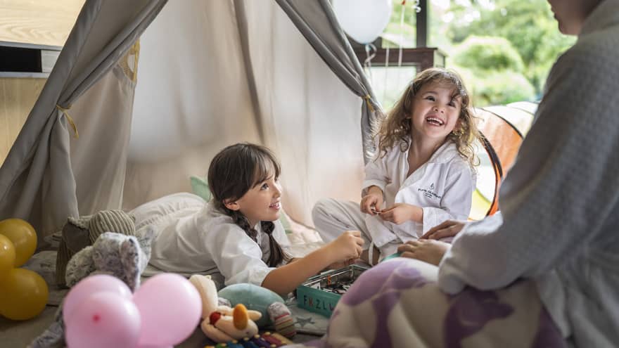 Two children in Four Seasons pajamas, smiling and playing together in a cozy indoor tent setup