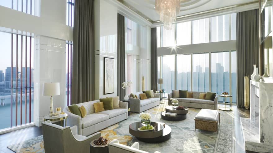 Royal Suite with high dome ceiling, modern crystal chandelier, sunny living room with several sofas and chairs, area rug