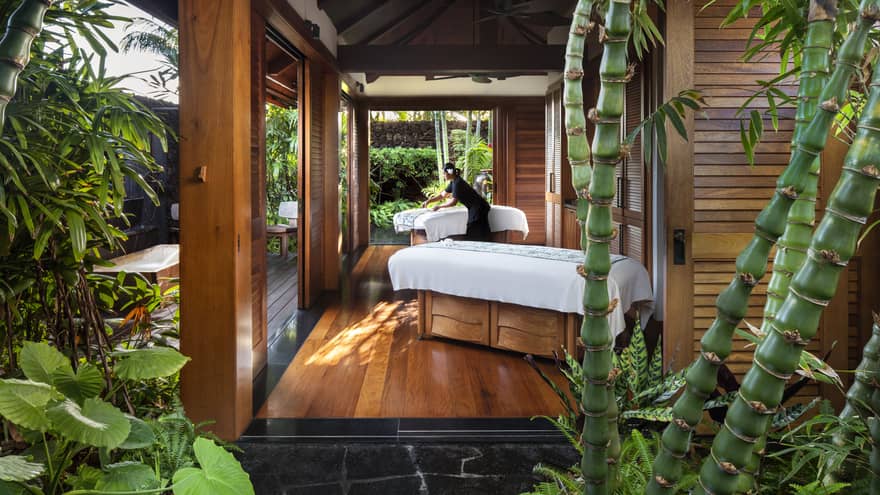 Spa staff spreads sheet on couples massage beds on open-air pavilion 