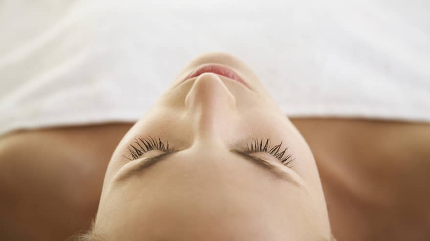 Woman lying down with eyes closed, bare shoulders, covered with white sheet