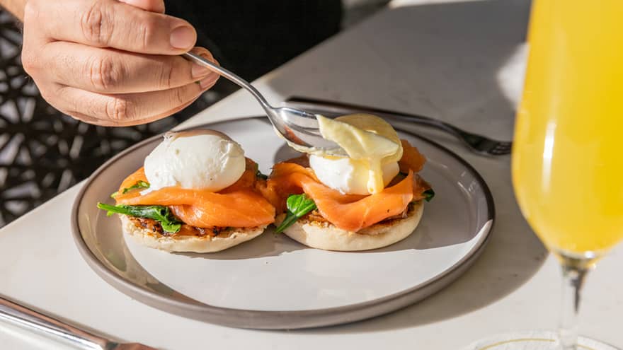 A person eating Eggs Benedict with silverware on the side