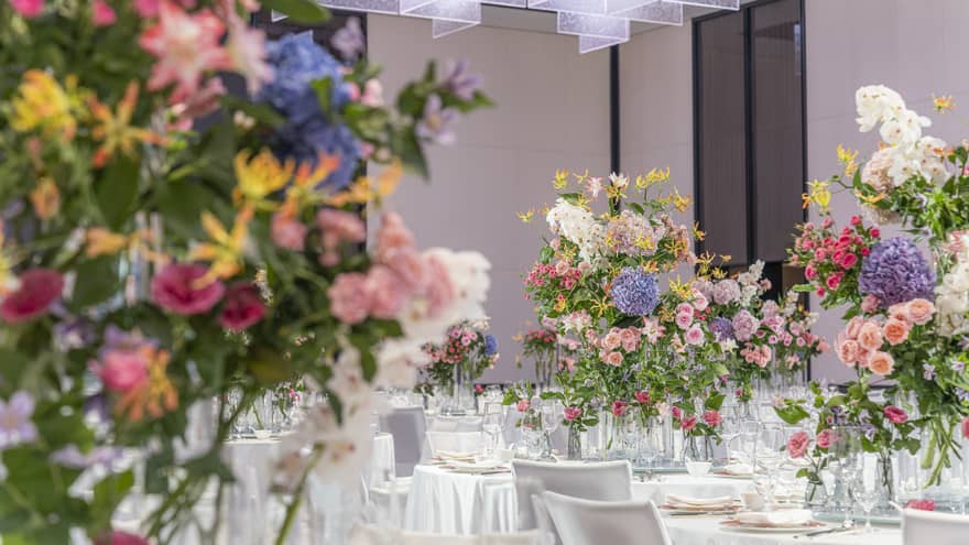 Hotel ballroom with banquet tables featuring large colourful floral arrangements
