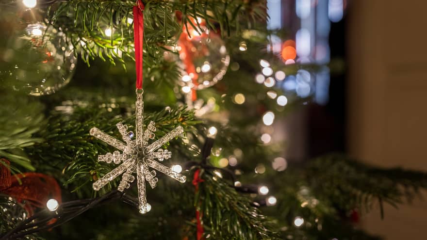 Close-up of a crystal snowflake ornament hanging on a Christmas tree with festive lights in the background
