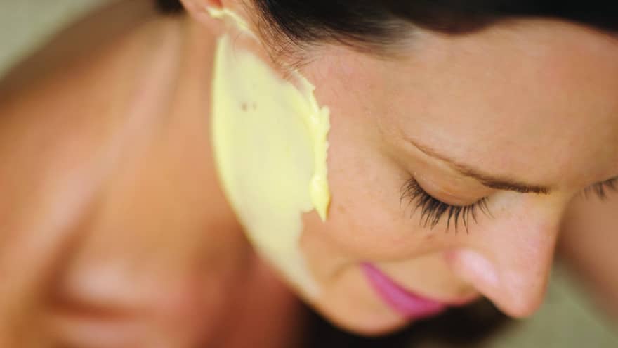 A close up of a woman looking down and smiling, with a yellow Sodashi Facial on her face
