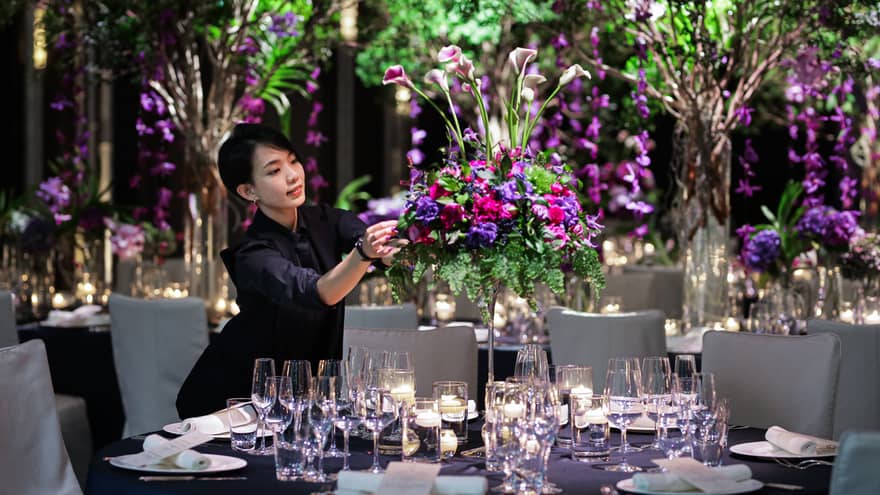 Wedding event staff arranges large floral centrepiece on banquet table