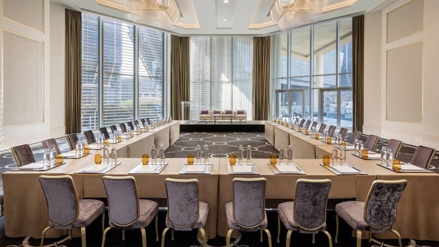 Meeting room with rectangular tables set up in a u-shape facing floor-to-ceiling windows