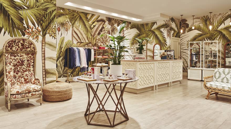 A brightly lit store with light wood features and clothes on shelves and hangers.