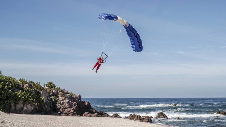 A man dressed in a Santa outfit in a parachute landing on the beach.