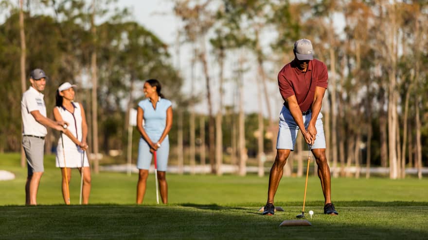 A man lines up a putt in the foreground while his wife and another couple laugh in the background at the golf course at four seasons orlando