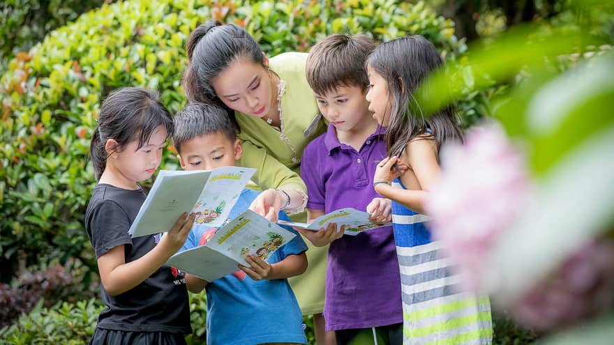 Children gather around hotel staff with treasure hunt kids activity pamphlets