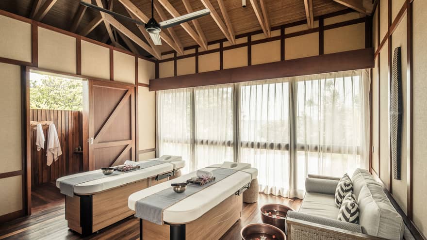 Two massage tables with copper bowls by wicker sofa, spa tubs