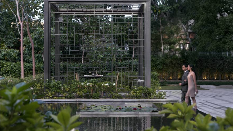 A couple walks through a dining area in a garden with lily pads and a waterfall