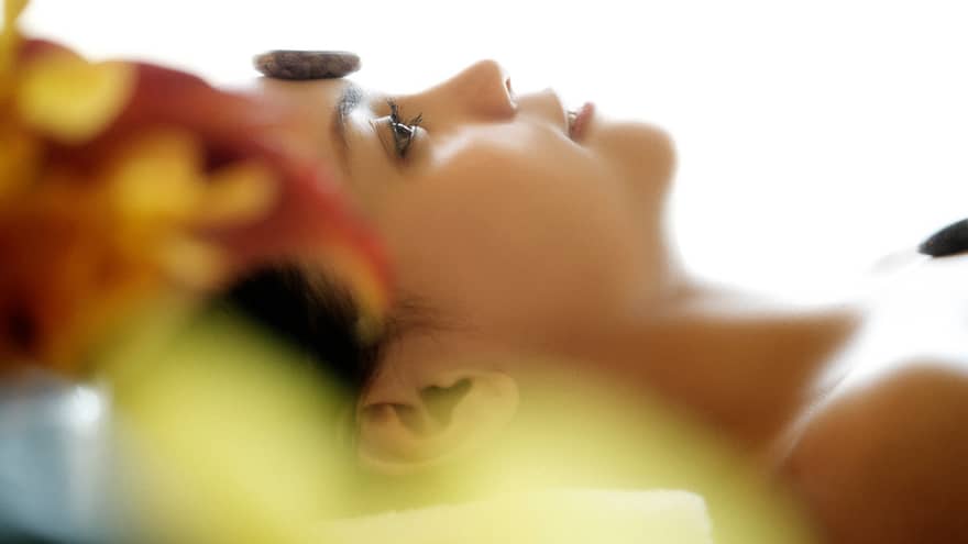Side of woman's face as she lies on spa table with small stone on forehead