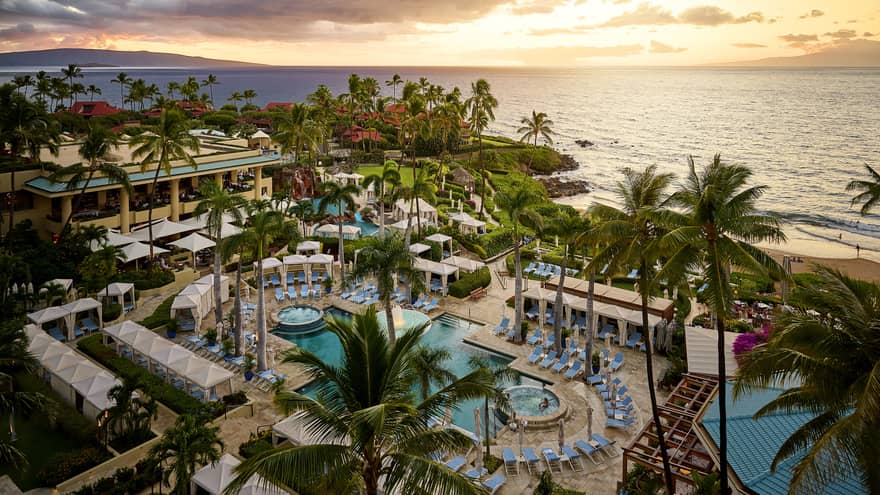 Aerial view of tropical resort with pools cabanas palm trees and ocean at sunset