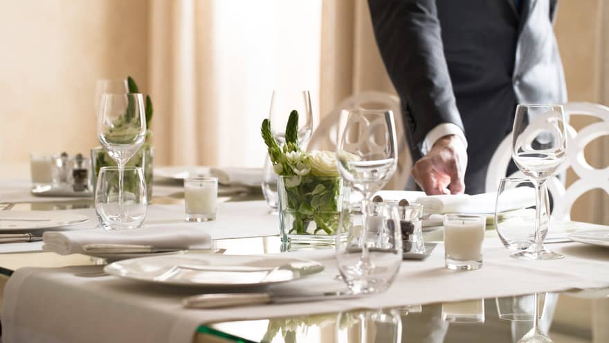 Hotel staff places napkin on small, elegant dining table in sunny room