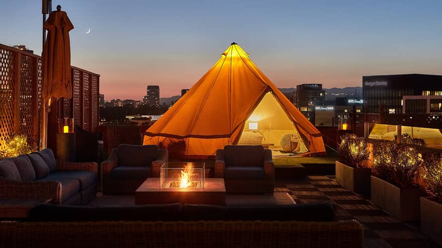 Close-up of illuminated white tent with bed, lamp by wicker chairs, modern outdoor fireplace