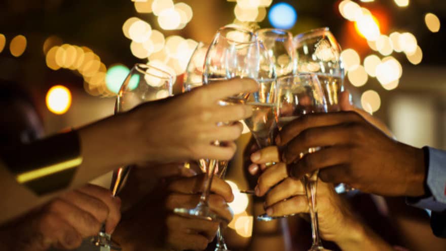 A group of guests clink their glasses of champagne together on a patio with twinkle lights