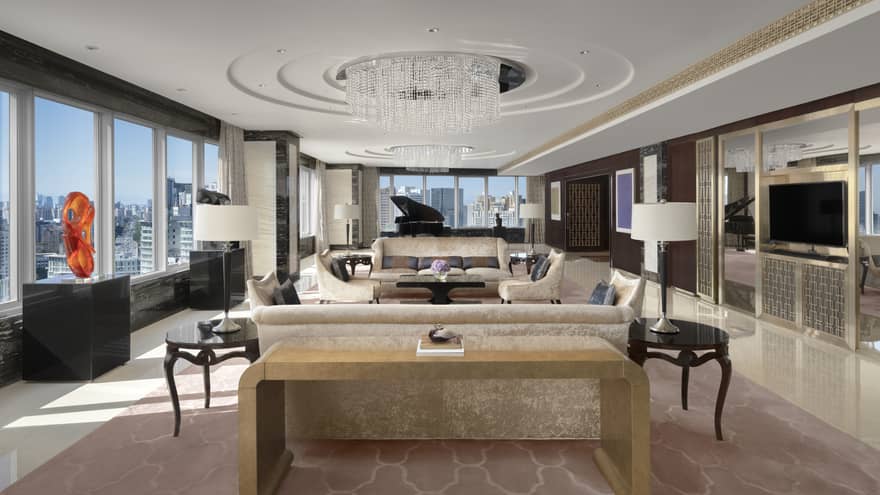 Lavish living room with circular chandelier, two sofas, red sculpture on display, walls of windows