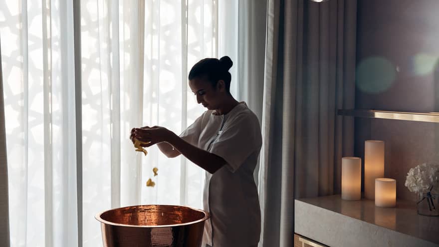 Spa therapist scatters flower petals into a copper basin